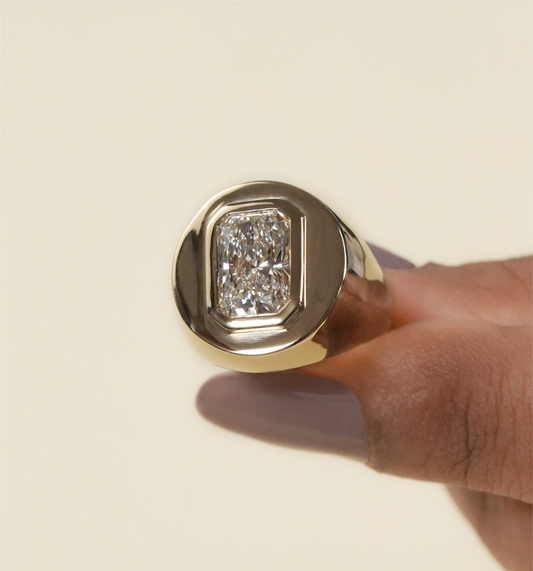 Gold ring with a diamond held by a hand on a beige background