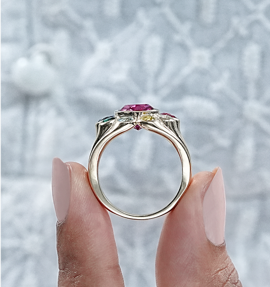 Gold ring with gemstones held by a hand against a light background