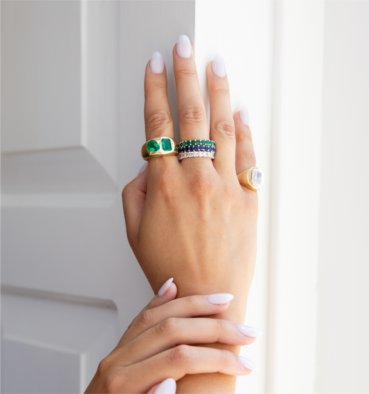 Hand wearing multiple rings with gemstones against a neutral background