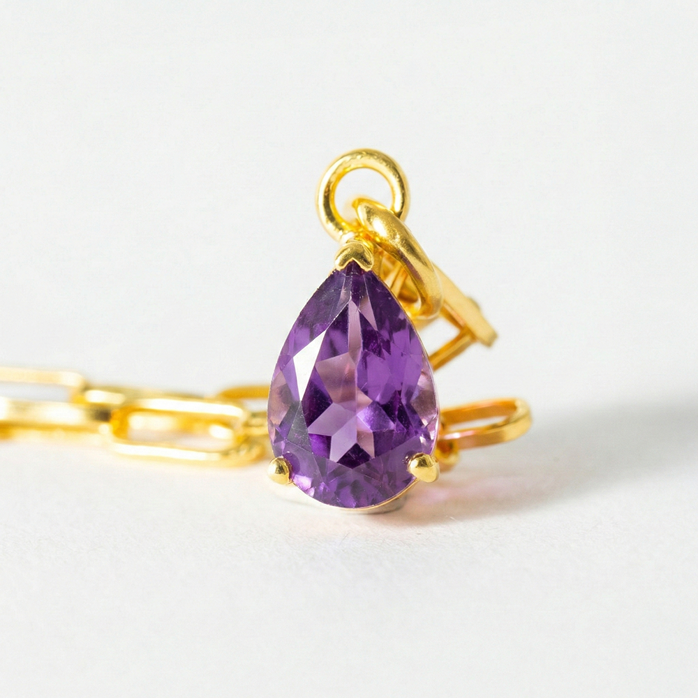 Gold necklace with a purple teardrop pendant on a white background