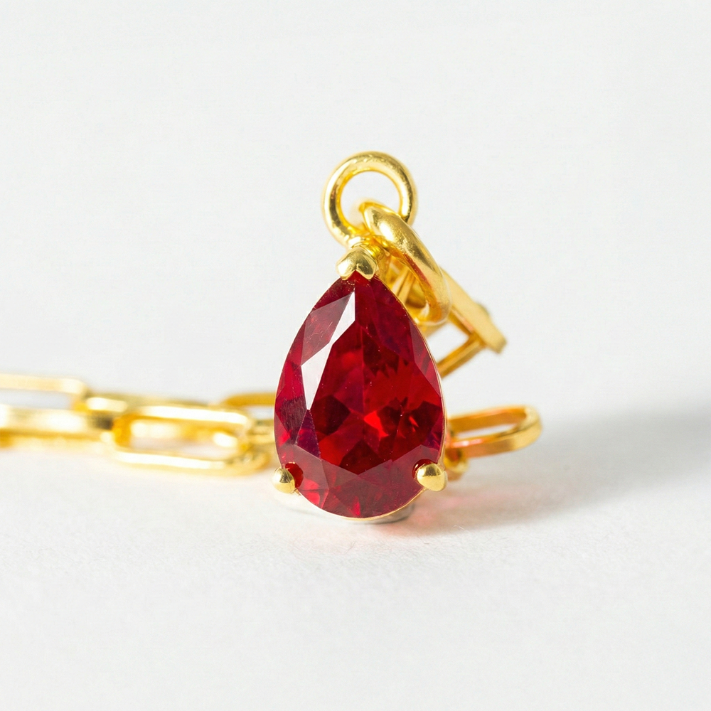 Gold ring with a red teardrop-shaped gemstone on a white background