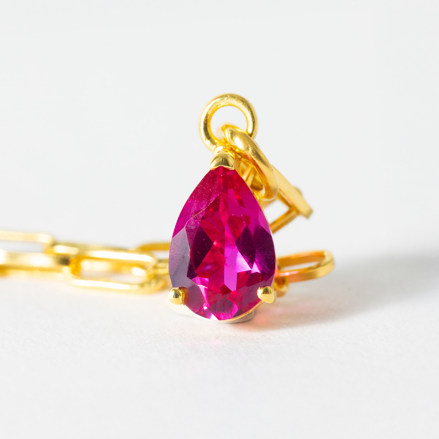 Gold chain with a pink teardrop pendant on a white background