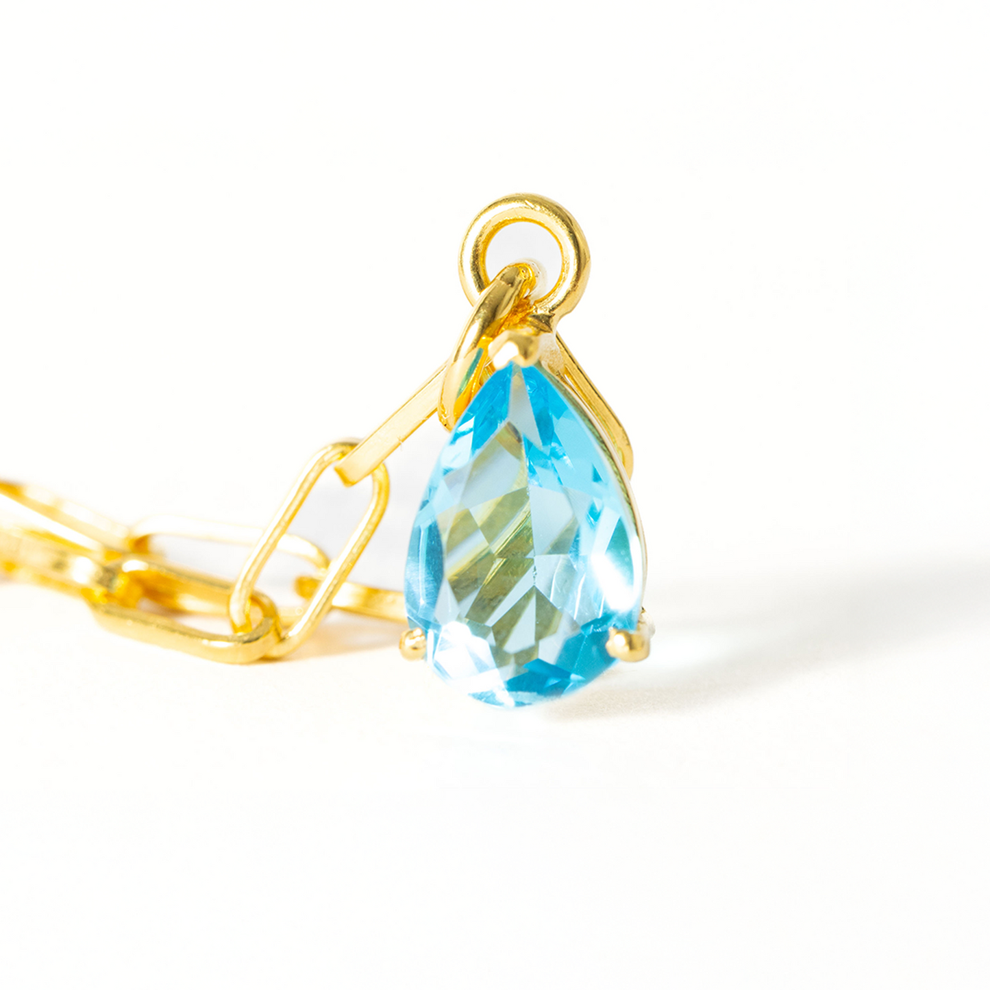 Gold necklace with a blue teardrop pendant on a white background