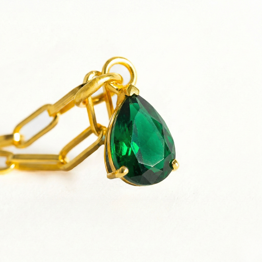 Gold chain with a green teardrop pendant on a white background