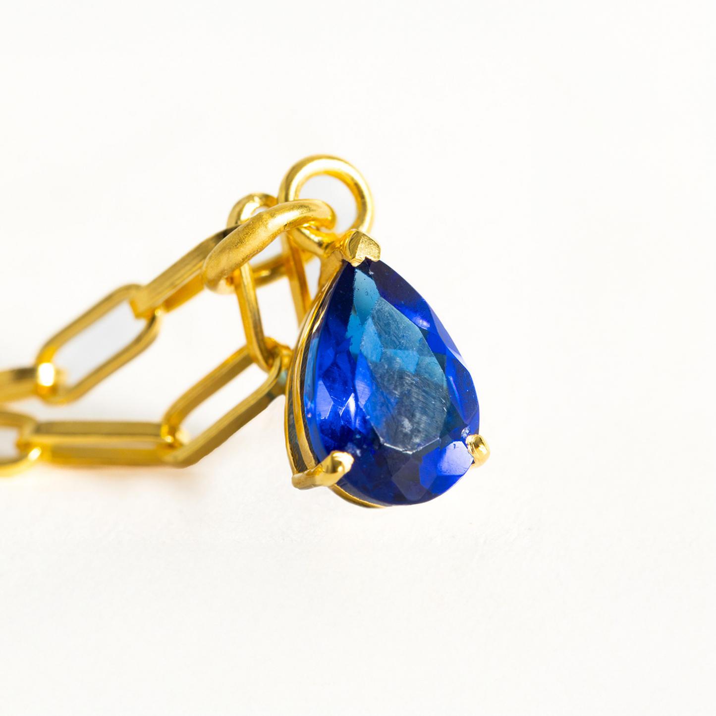 Gold chain with a blue teardrop pendant on a white background