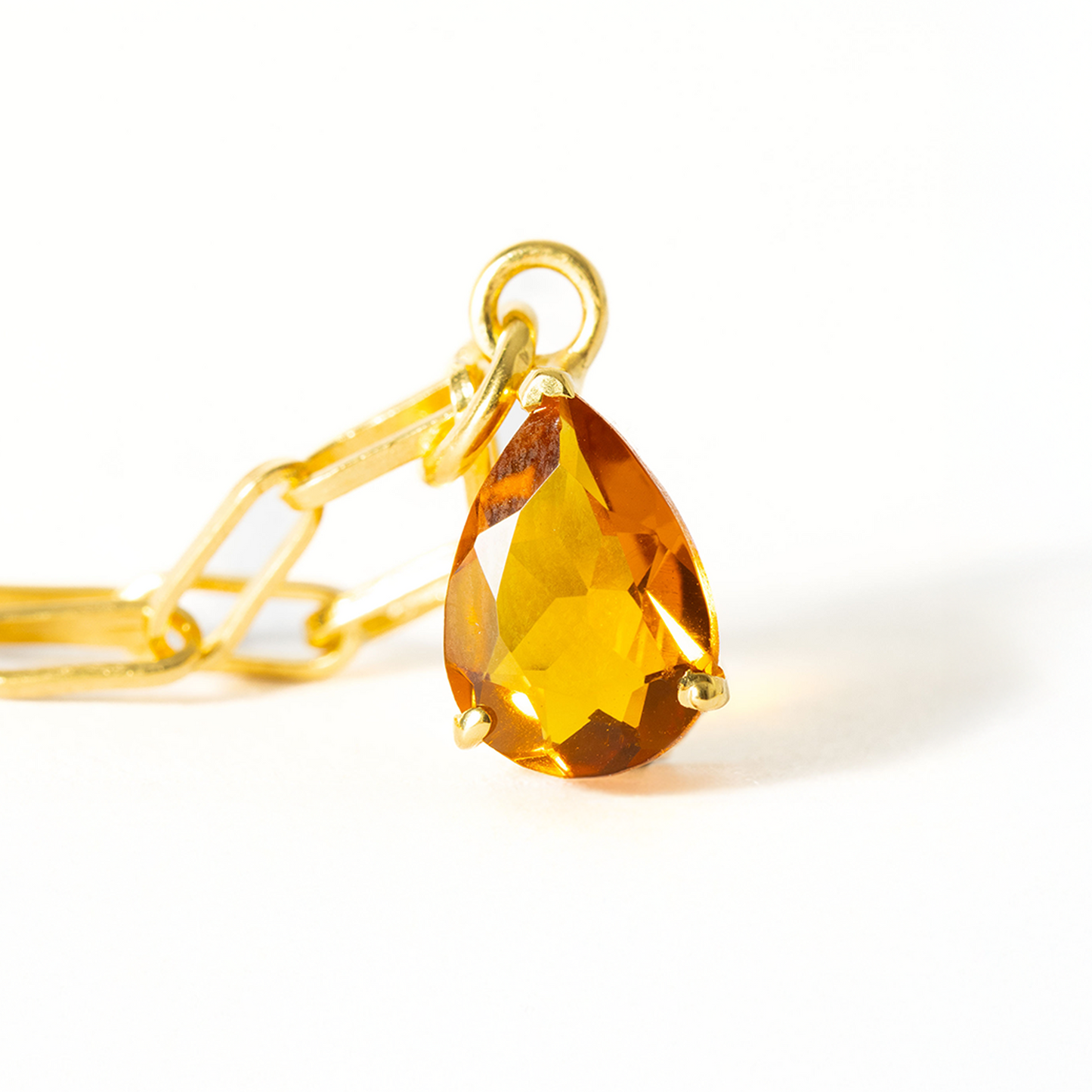 Gold pendant with a teardrop-shaped yellow gemstone on a white background