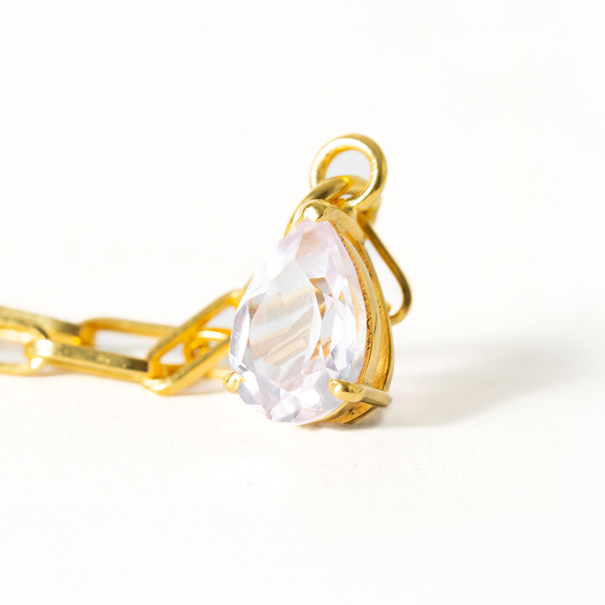 Gold necklace with a clear teardrop-shaped pendant on a white background