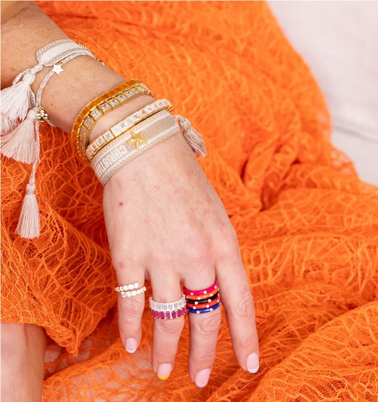 Hand wearing multiple bracelets and rings on an orange fabric background