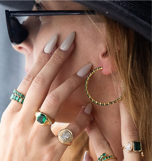 Close-up of a person wearing gold hoop earrings and multiple rings with gemstones.