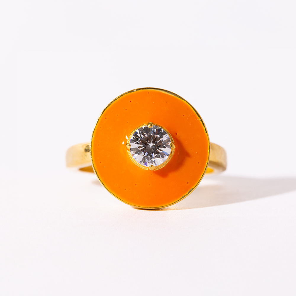 Ring with orange circular band and clear gemstone on a white background