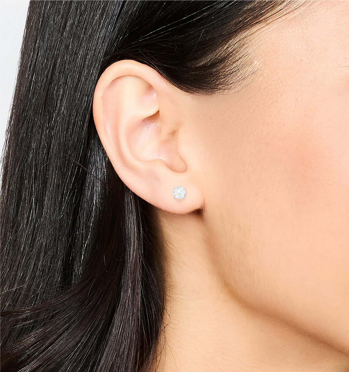 Close-up of an ear wearing a silver earring with a clear gemstone.