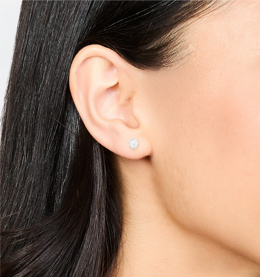 Close-up of an ear wearing a silver earring with a clear gemstone.