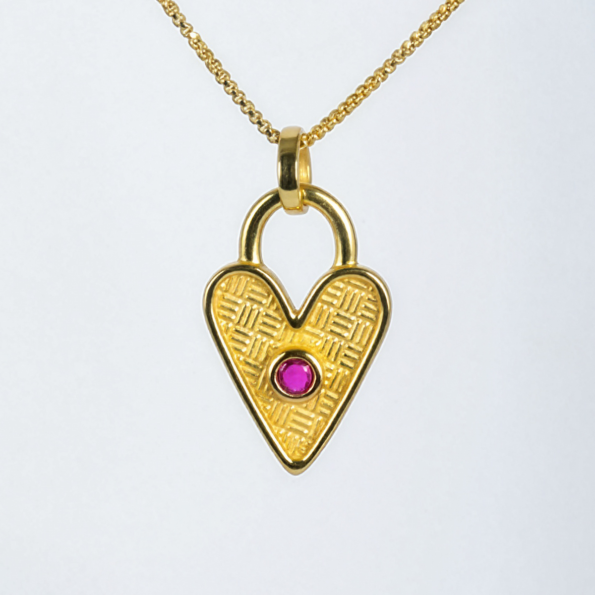 Gold heart-shaped pendant with a red gemstone on a white background