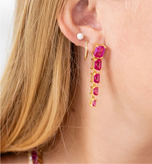 Close-up of a person wearing gold earrings with pink gemstones and a small diamond earring.