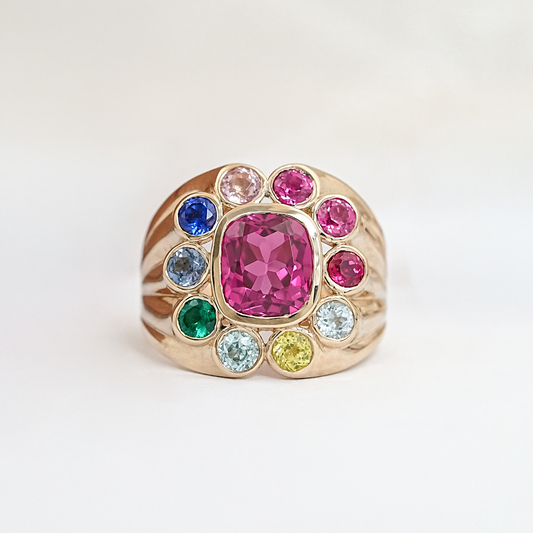 Ring with a pink gemstone surrounded by smaller colored gems on a light background