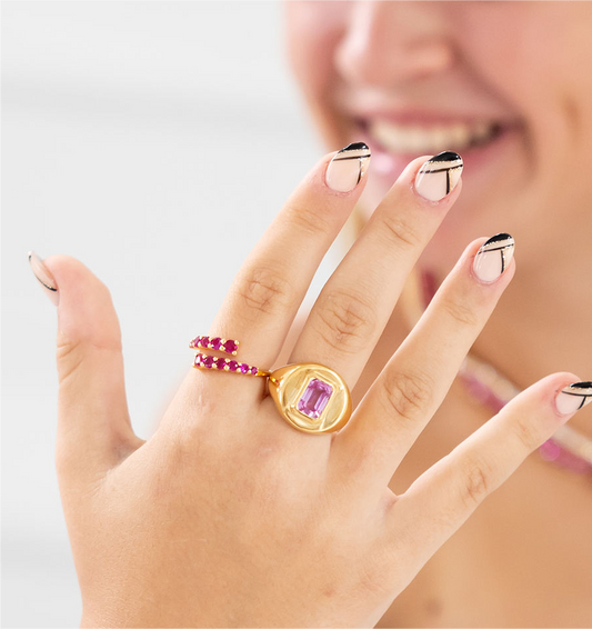 Close-up of a hand wearing a gold ring with a pink gemstone on a light background
