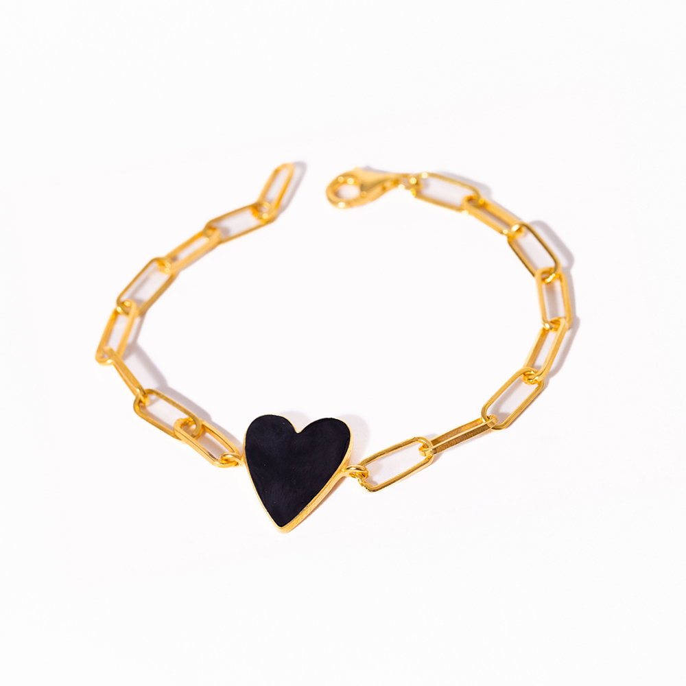 Gold chain bracelet with a black heart charm on a white background