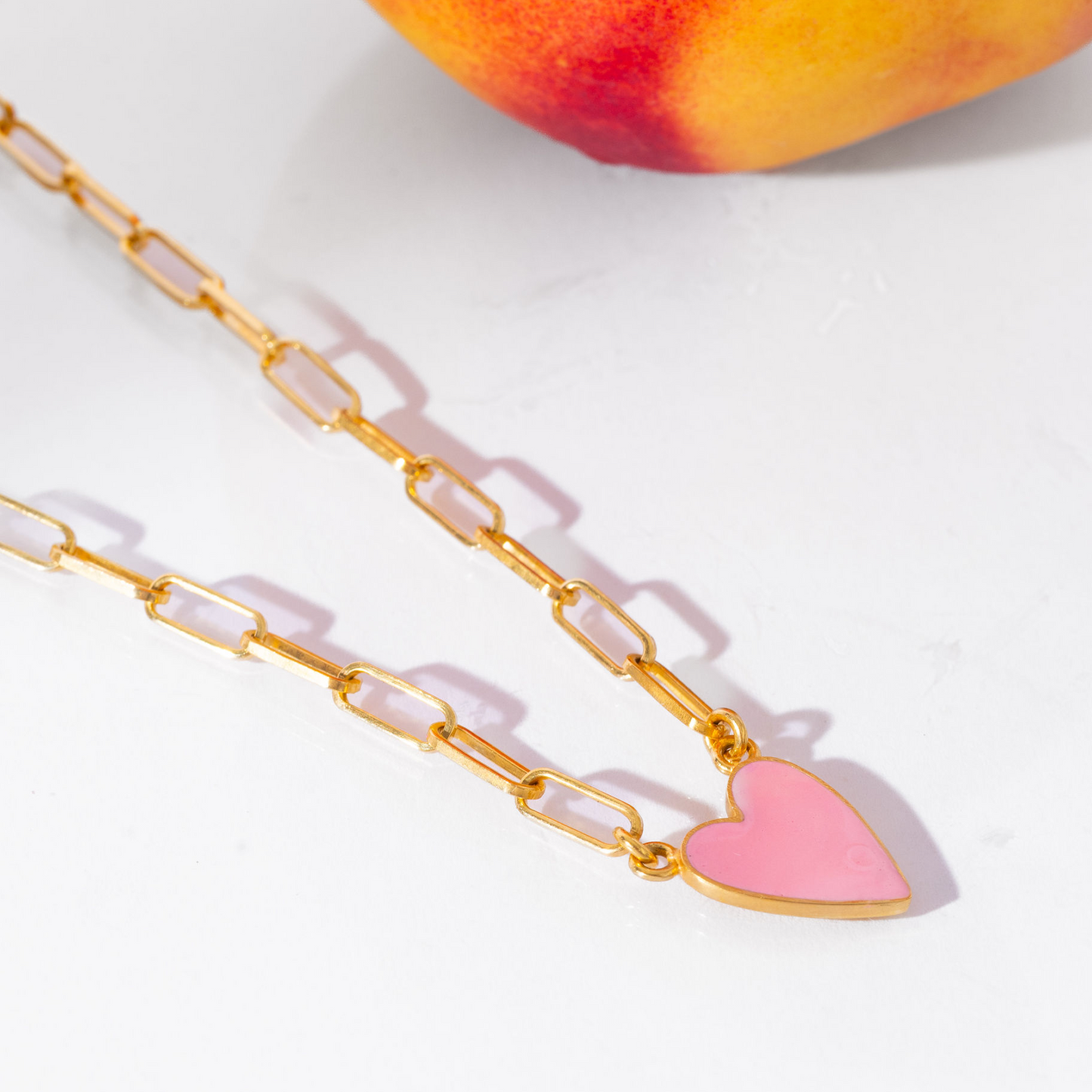 Gold chain necklace with a pink heart pendant on a white background