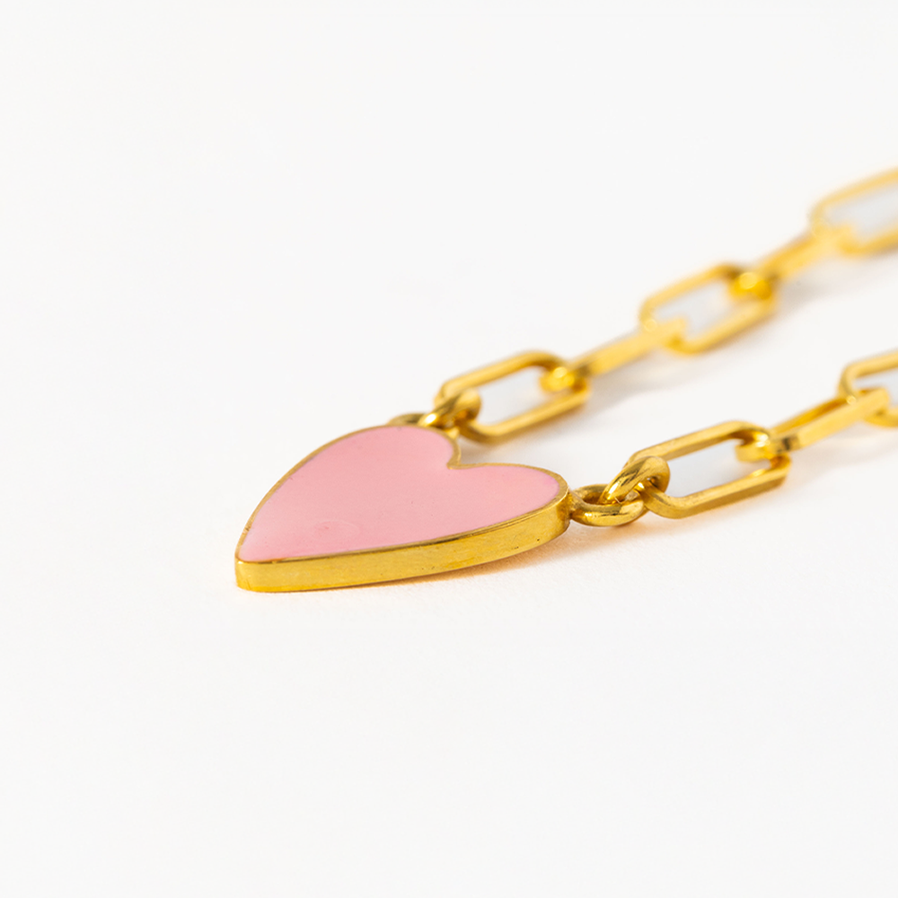 Gold chain bracelet with a pink heart charm on a white background